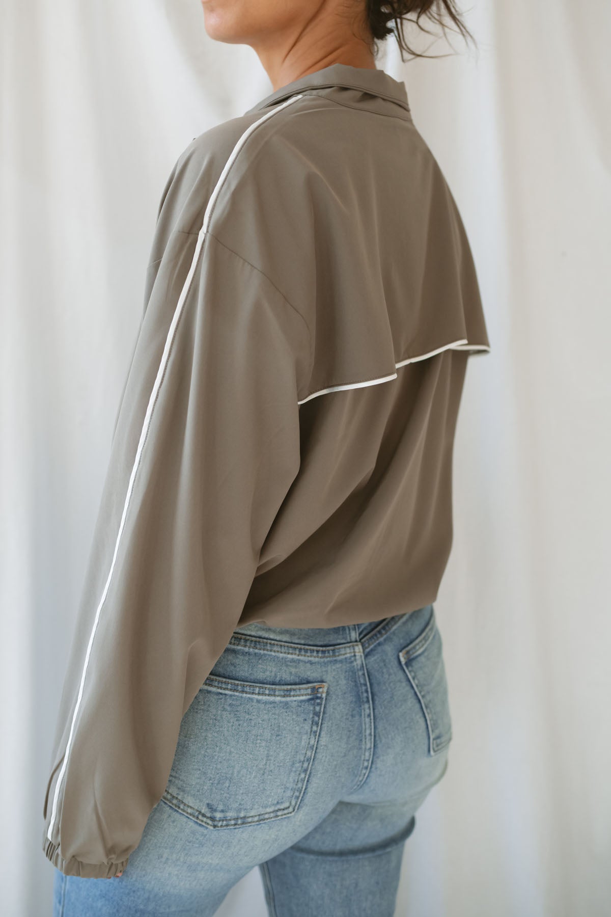 Women with dark hair wearing the truffle active jack with full zip front and pipping detail on the sleeve wearing jeans and standing in front of a white background.