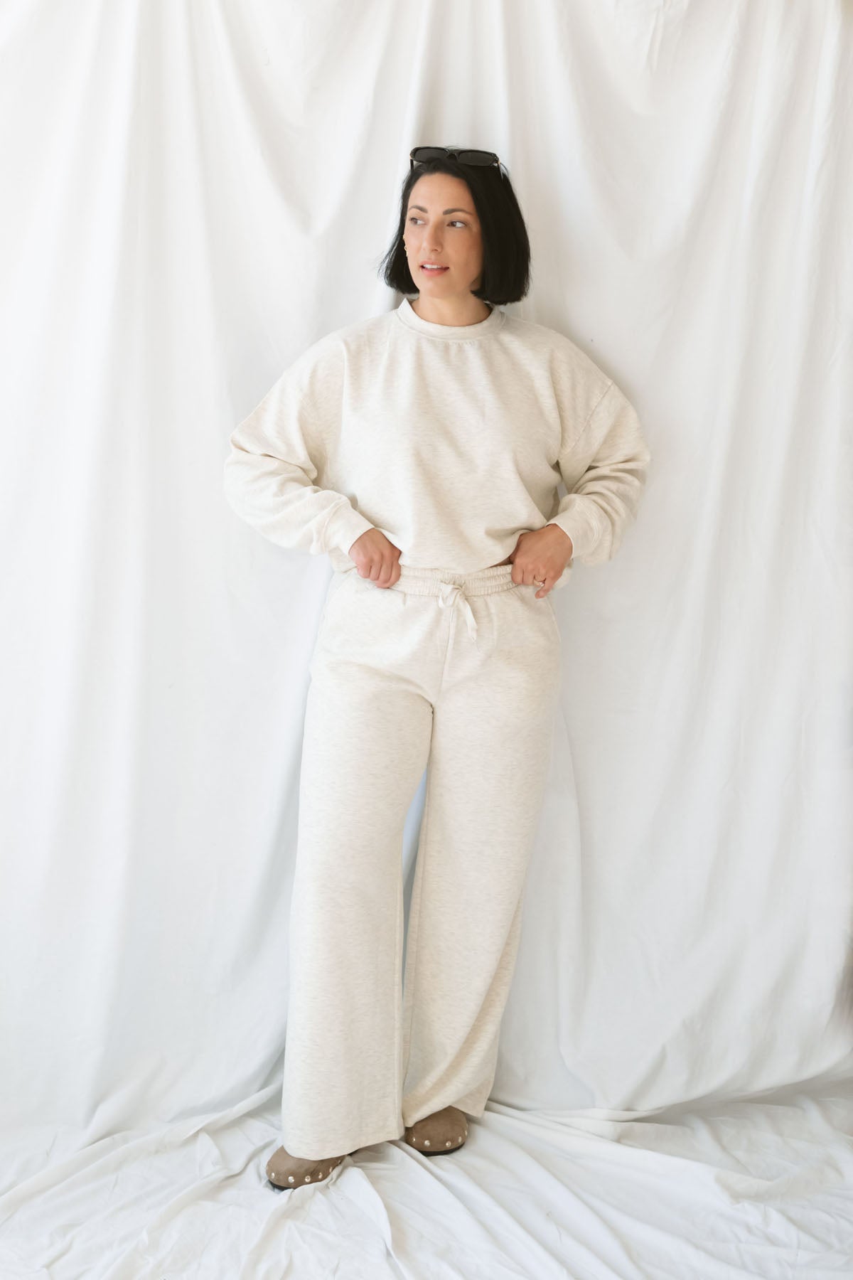 Woman wearing a light beige lounge set with crew neck sweatshirt and drawstring pants on a white background