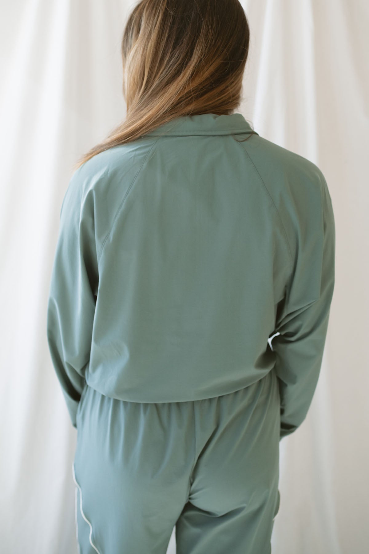 Woman with light brown hair wearing a eucalyptus half zip active jacket with collar wearing matching pants on a white background