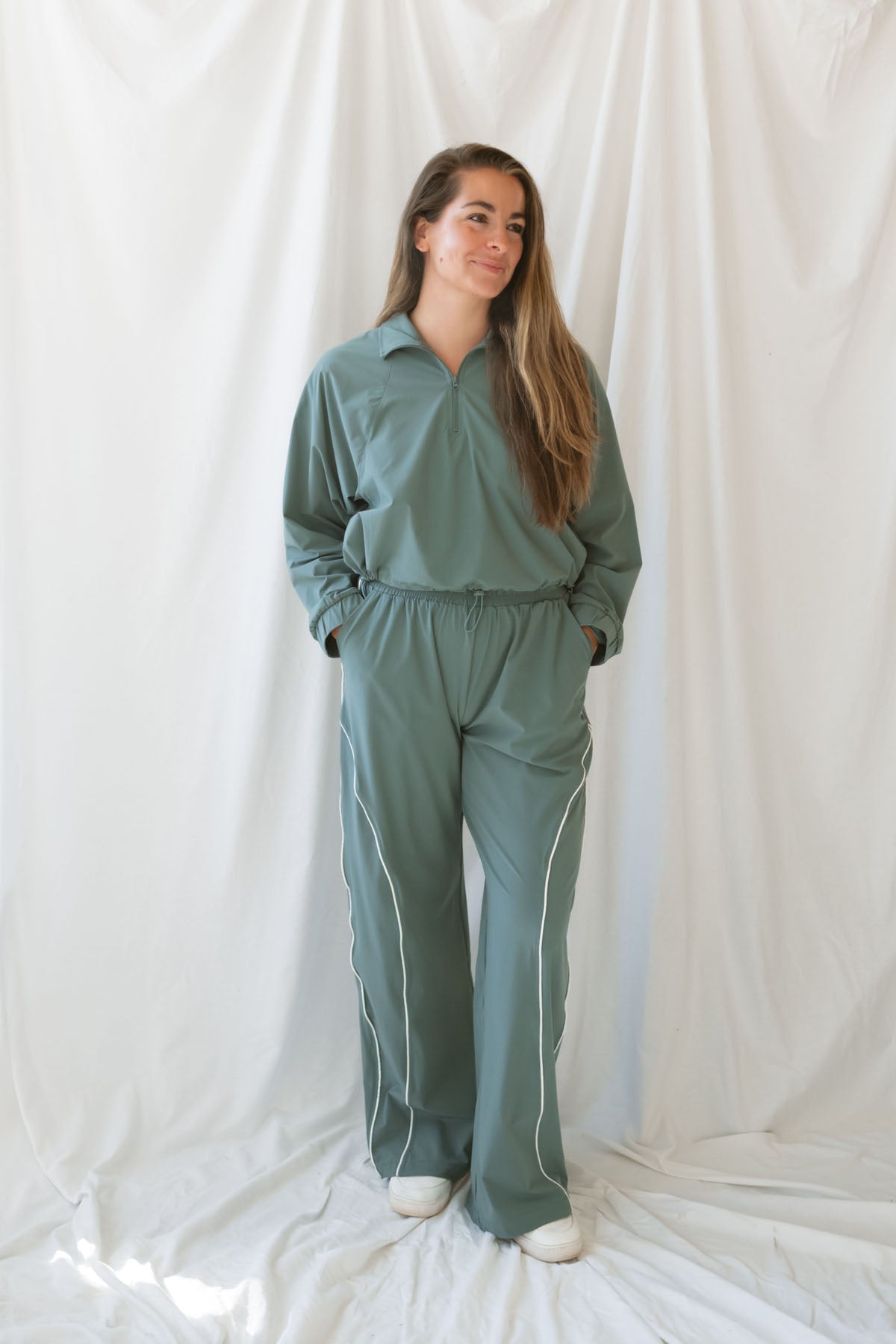 Woman wearing eucalyptus green wide-leg track pants with white contrast piping and an elastic drawstring waistband.