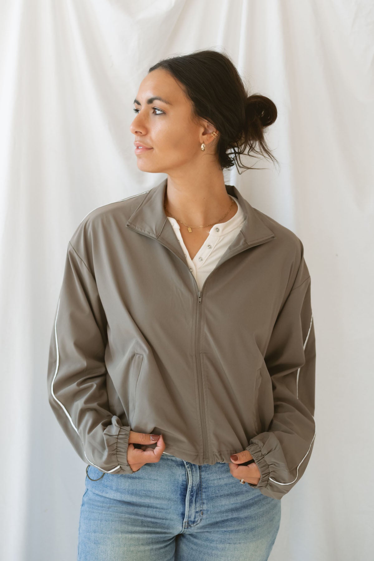 Women with dark hair wearing the truffle active jack with full zip front and pipping detail on the sleeve wearing jeans and standing in front of a white background.