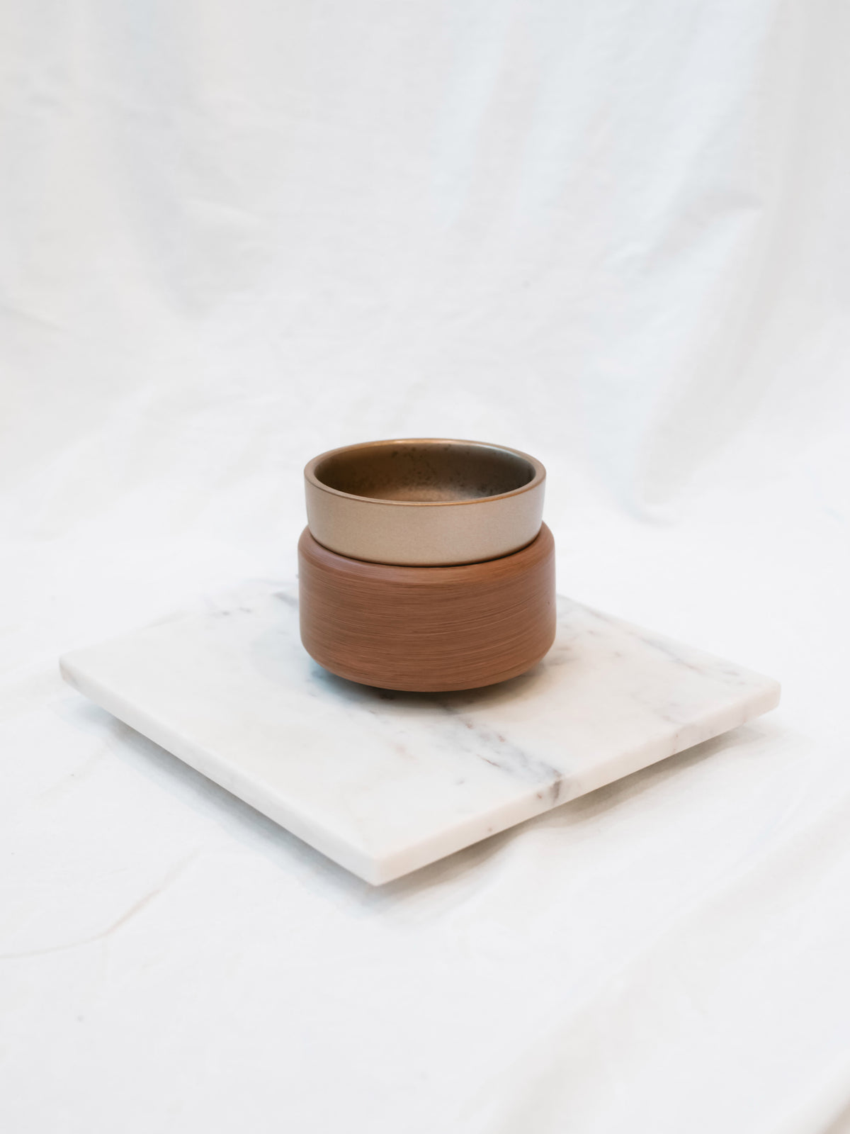Pewter and walnut detailed wax warmer on a marble riser in front of a white background