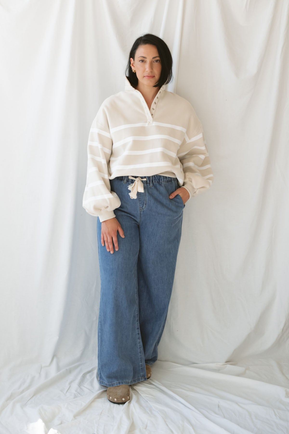 Woman wearing wide leg medium wash denim with drawstring waistband with taupe sweatshirt on a white background.