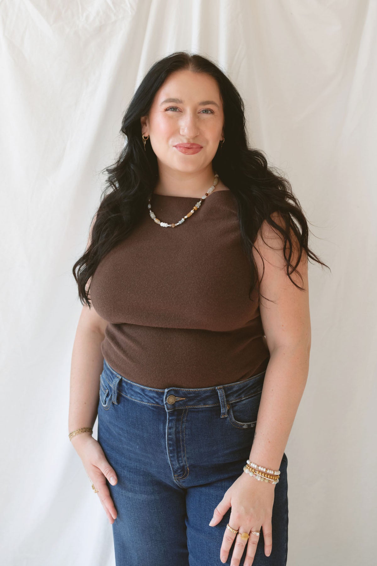Model wearing the asymmetrical knit sweater sleeveless top with a dark pair of denim for a late summer early fall transition outfit.