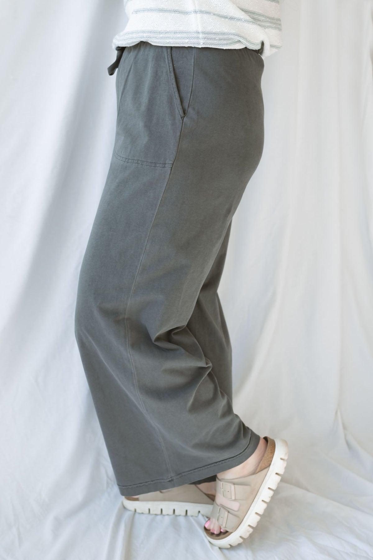 Side view of model wearing cotton wide leg pants with drawstring waistband. Model has the pants styled with a lightweight sweater, but they can be paired with other basics tees or blouses.