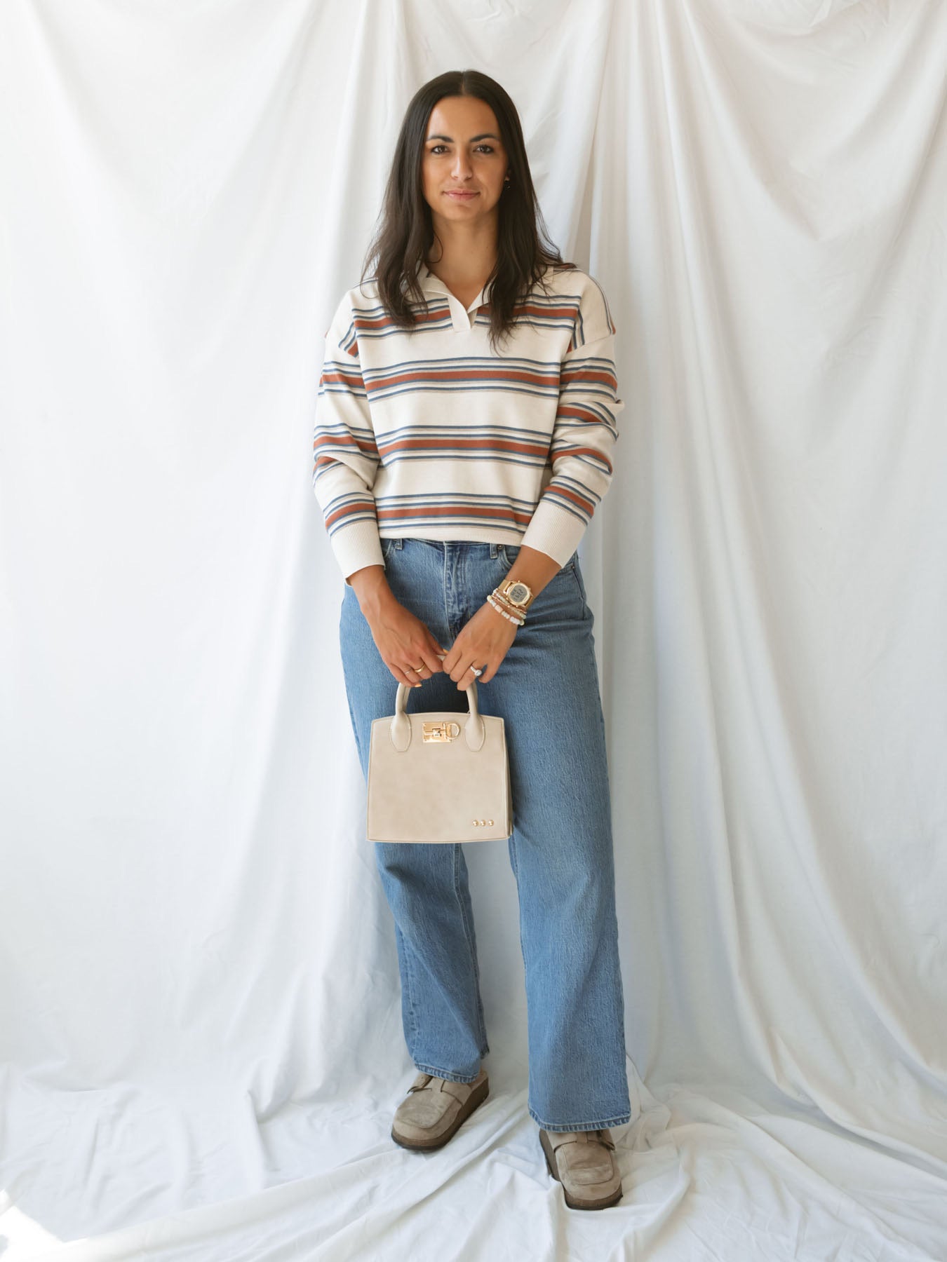 Model holding small nixie tote bag with top handle and metal fastened detail.