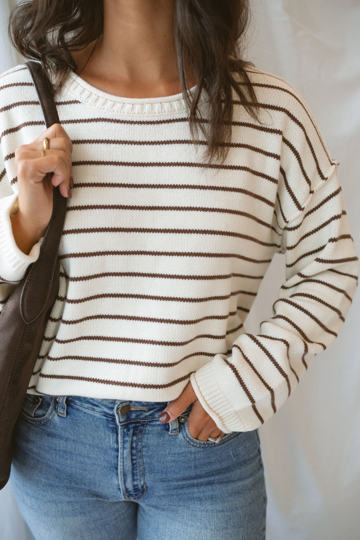 Model wearing striped crew neck sweater with raw edge detail.