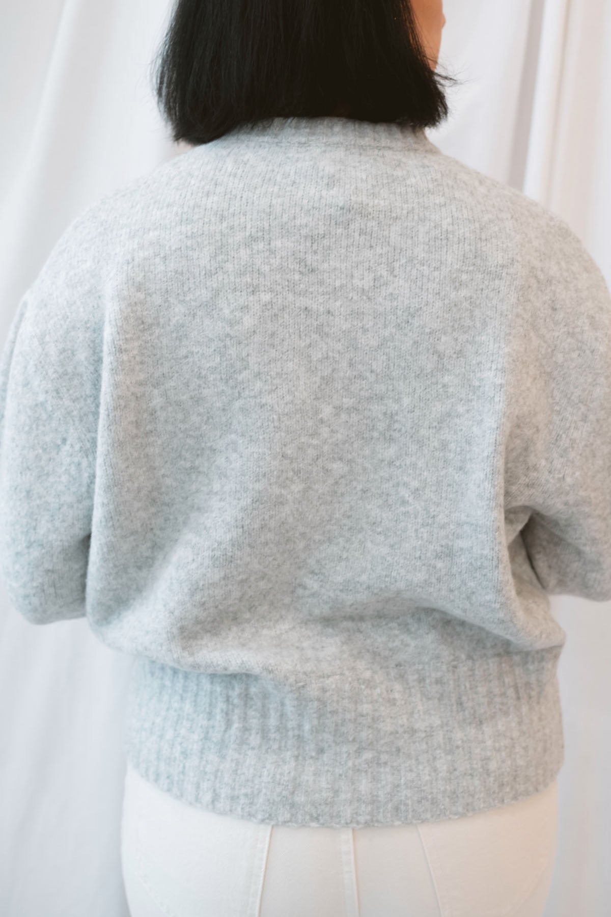 Model is wearing solid heather grey crew neck sweater. Styled with cream twist barrel pants.