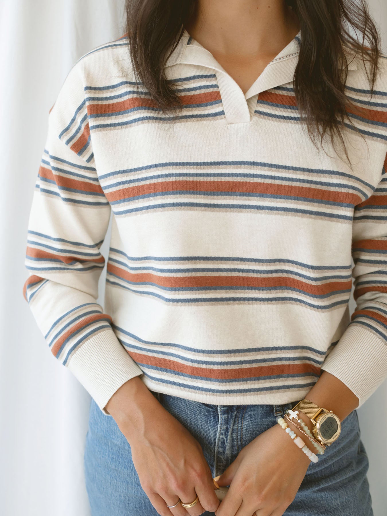 Model wearing the collared striped polo sweater. Off white, rust, and teal give this shirt a retro vibe while still bringing a modern twist.