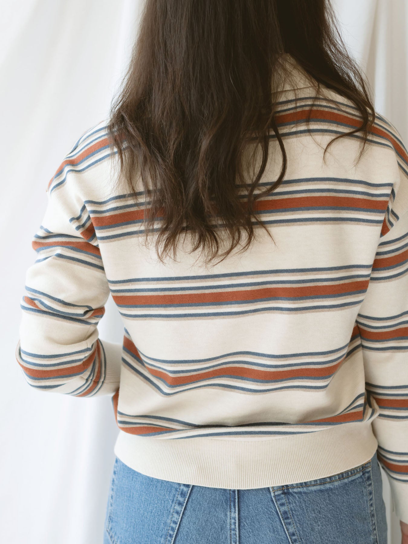 Model wearing the collared striped polo sweater. Off white, rust, and teal give this shirt a retro vibe while still bringing a modern twist.
