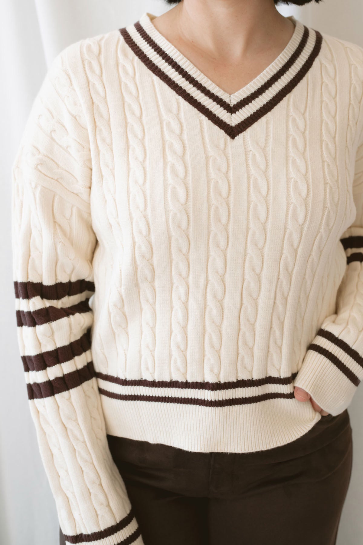 Charlotte cream cable knit V-neck varsity sweater with chocolate brown accents and classic collegiate-inspired details.