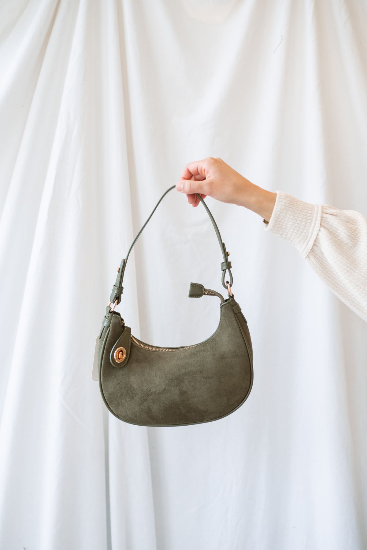 Model holding the olive green faux suede shoulder bag with gold hardware.