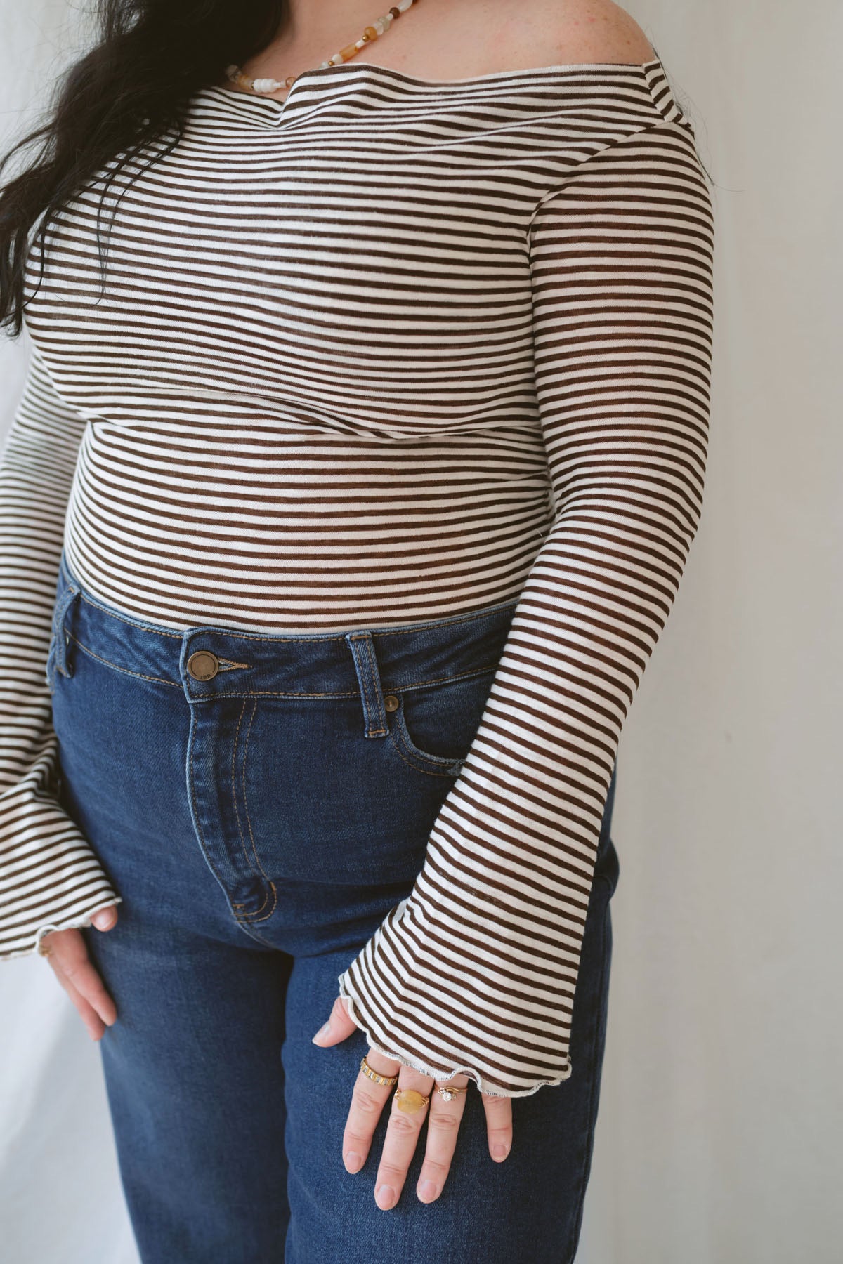 Model wearing the asymmetrical off the shoulder striped top with a pair of basic dark denim and a pop of color in the necklace. Top has lettuce hem detail on the sleeves and a fitted look.