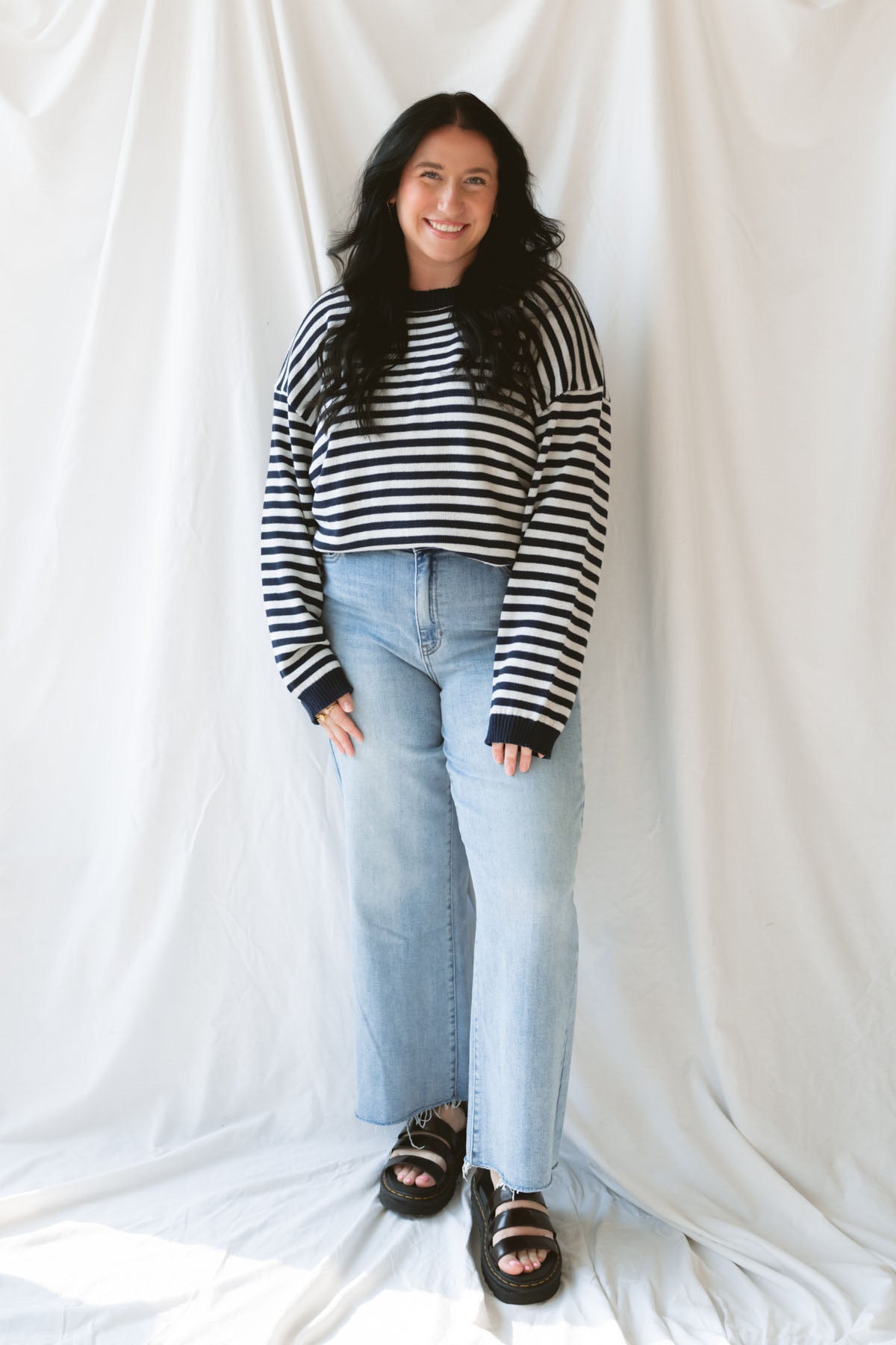 Model wearing striped lightweight sweater with back button detail. Hem stands out with a thicker band of the deep navy, contrasting the white beautifully. Model has sweater pairs with a classic pair of jeans.