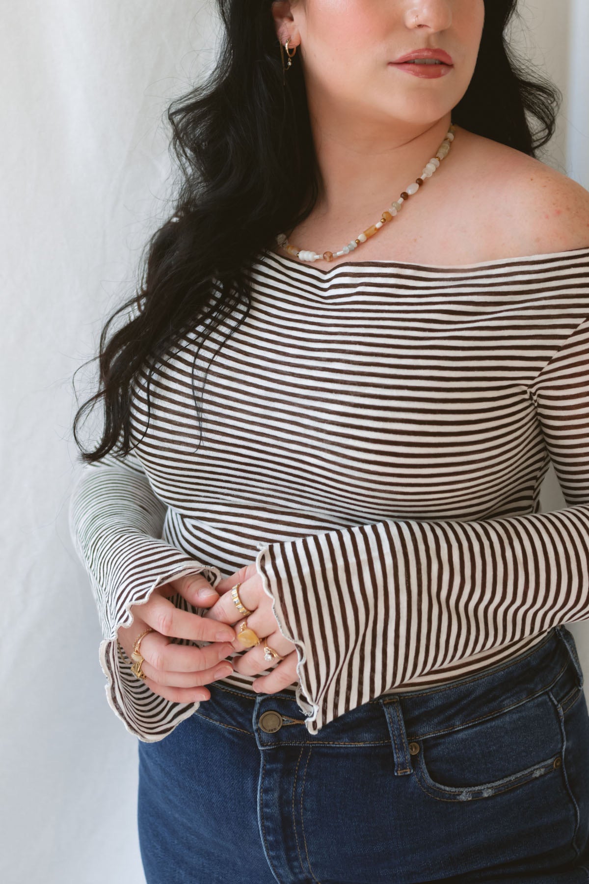 Model wearing the asymmetrical off the shoulder striped top with a pair of basic dark denim and a pop of color in the necklace. Top has lettuce hem detail on the sleeves and a fitted look.