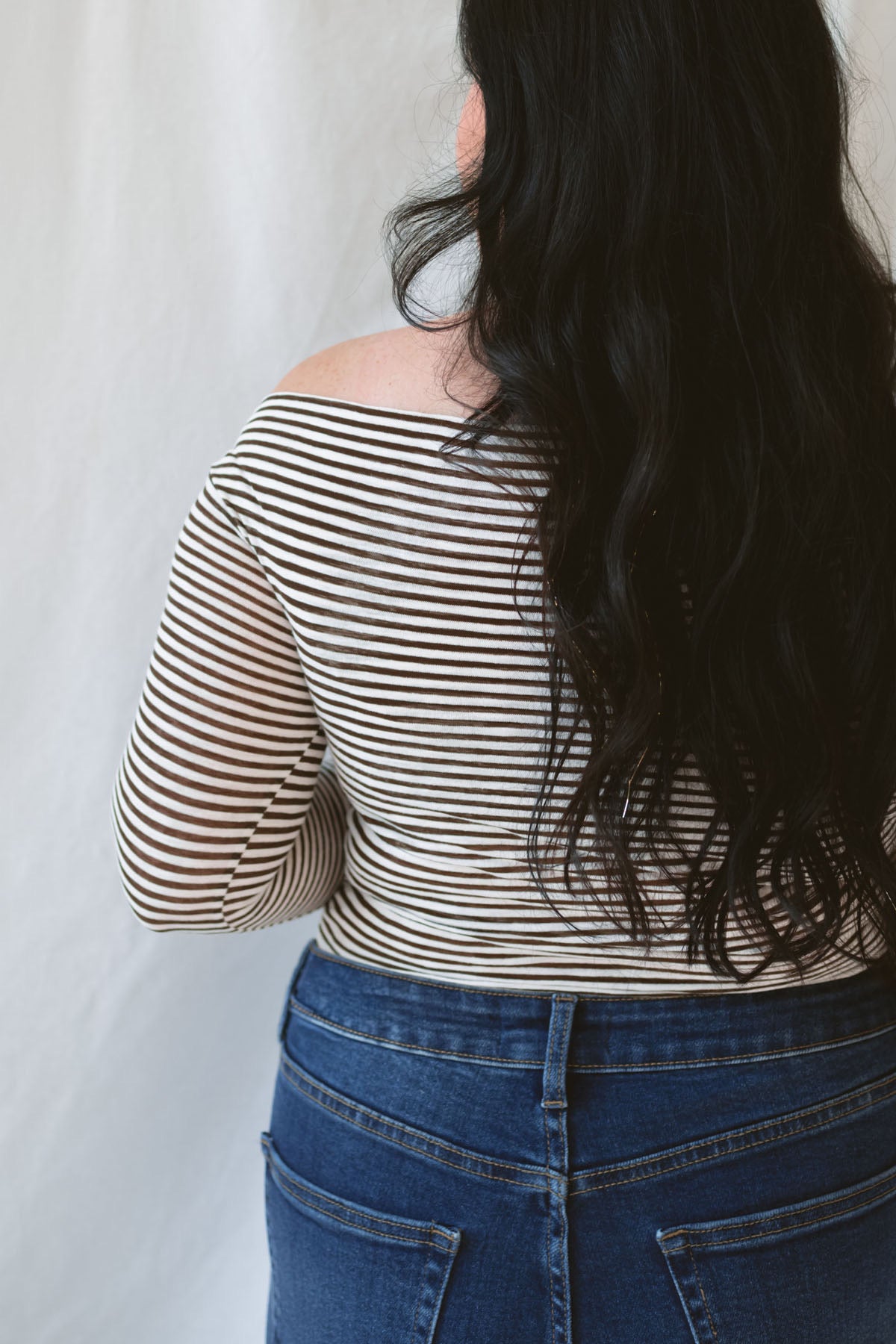 Model wearing the asymmetrical off the shoulder striped top with a pair of basic dark denim and a pop of color in the necklace. Top has lettuce hem detail on the sleeves and a fitted look.