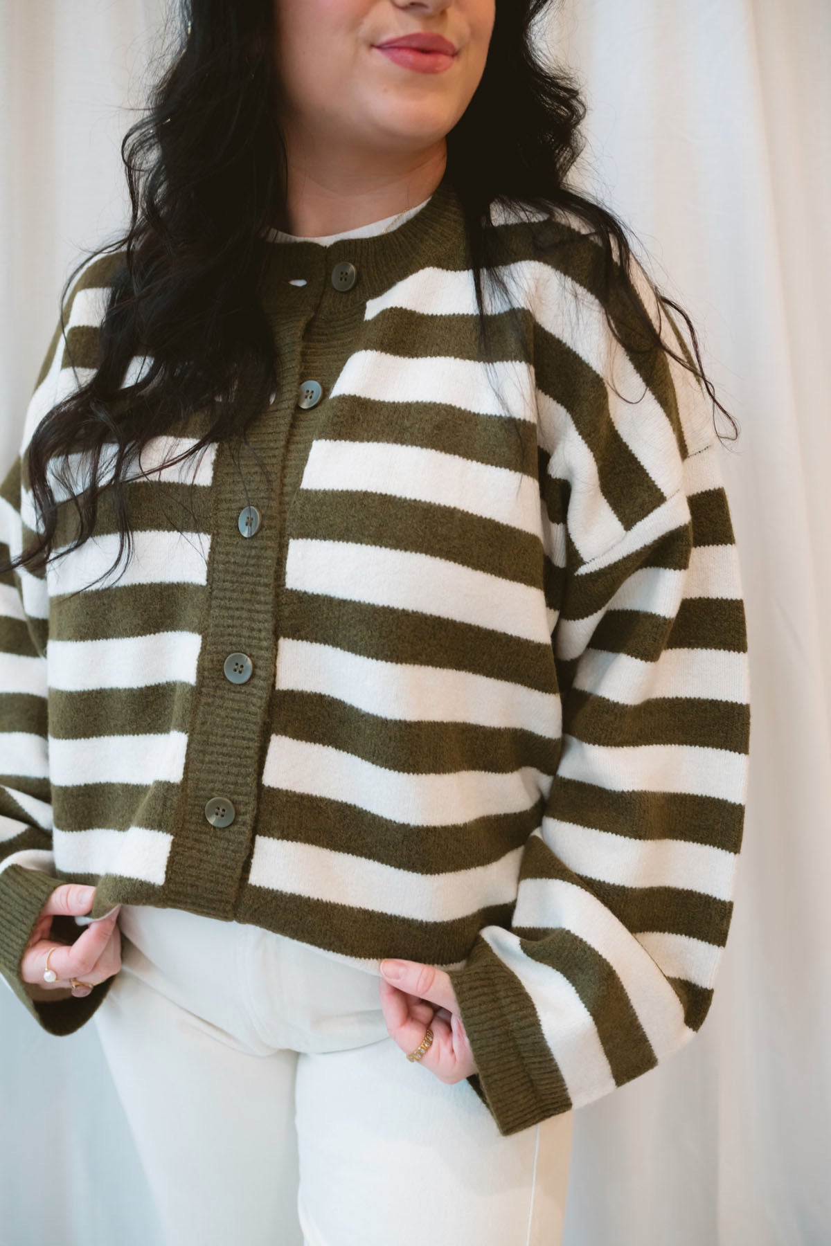 Model is wearing oversized striped button down cardigan in olive and cream.