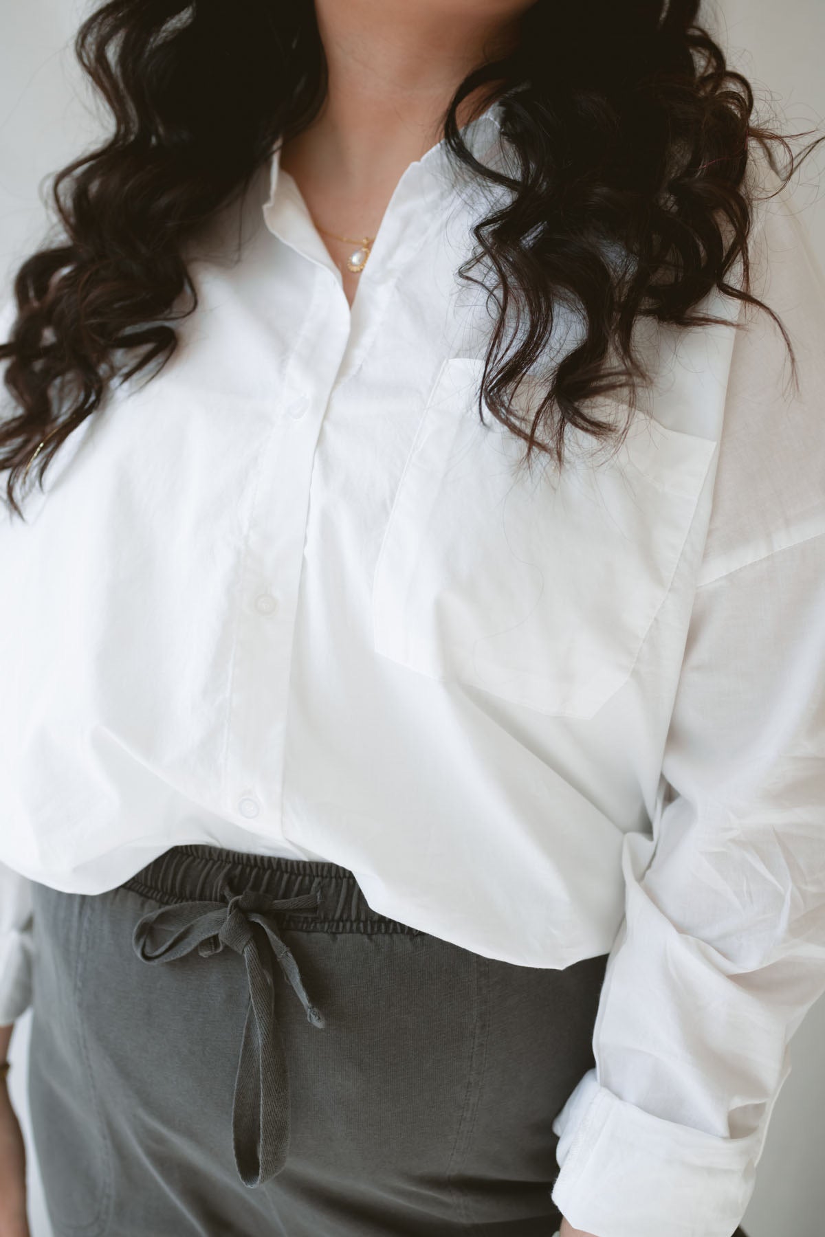Close up of model wearing the long sleeve white button up top. Model has shirt styled fully buttoned and tucked into the Mila wide leg pants. This outfit is easy and casual but still feels put together.