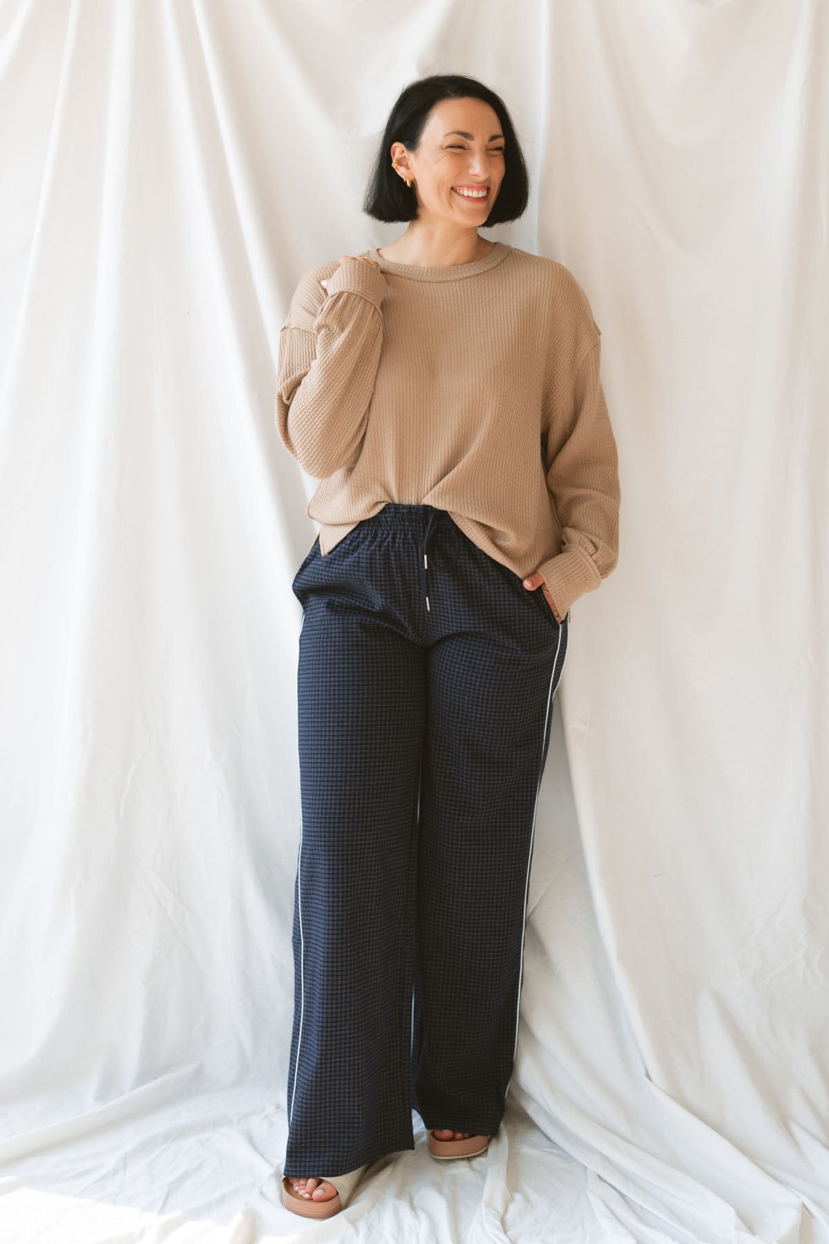 Model wearing textured exposed seam long sleeve top in color khaki. A great basic to dress up or down with a variety of pant styles. Model styled with our checkered drawstring waist pants in navy for a beautiful color combination and comfortable feel.