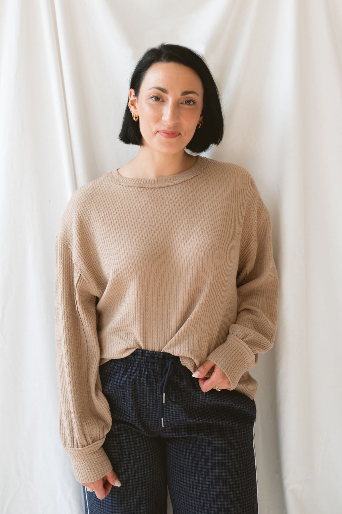 Model wearing textured exposed seam long sleeve top in color khaki. A great basic to dress up or down with a variety of pant styles. Model styled with our checkered drawstring waist pants in navy for a beautiful color combination and comfortable feel.