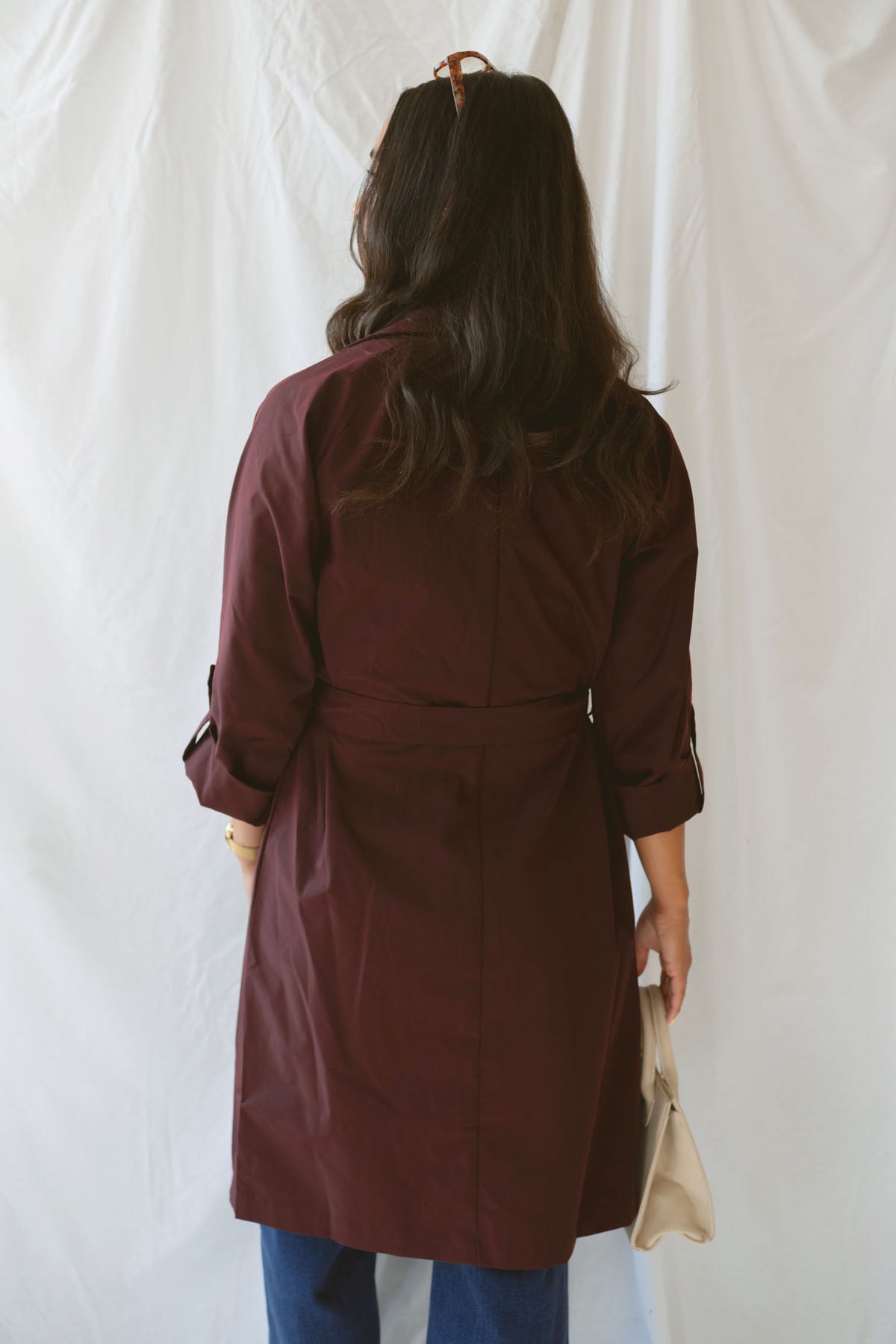 Model showing the back side of the maroon trench coat with tie waist detail.