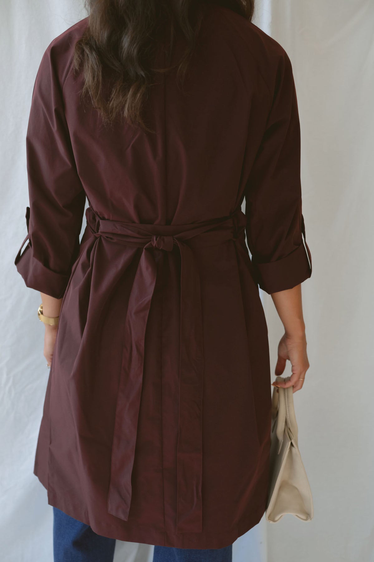 Model showing the back side of the maroon trench coat with tie waist detail.
