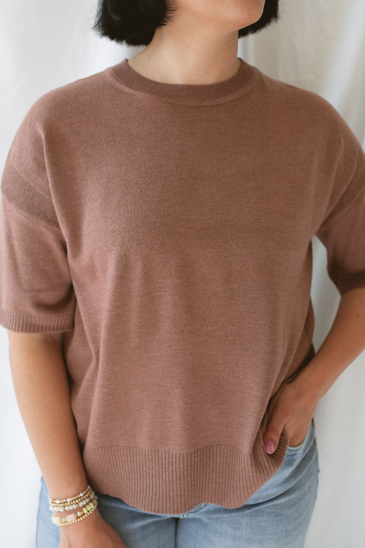 Close up view of model wearing the boxy fit short sleeve sweater in a rusty rose / sepia color. Model paired the top with jeans and a platform sandal. Wears well through seasons.