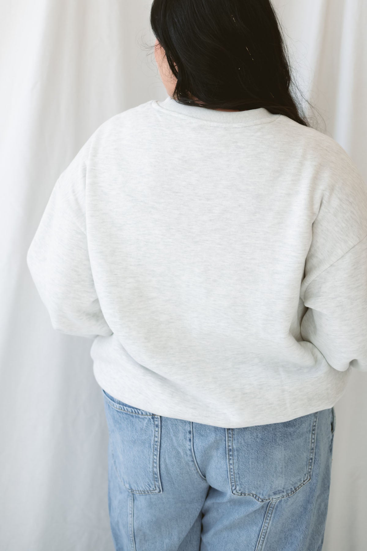 Model wearing the oversized grey crew neck sweatshirt. Model has it styled with a pair of barrel jeans and sneakers for a casual everyday look.