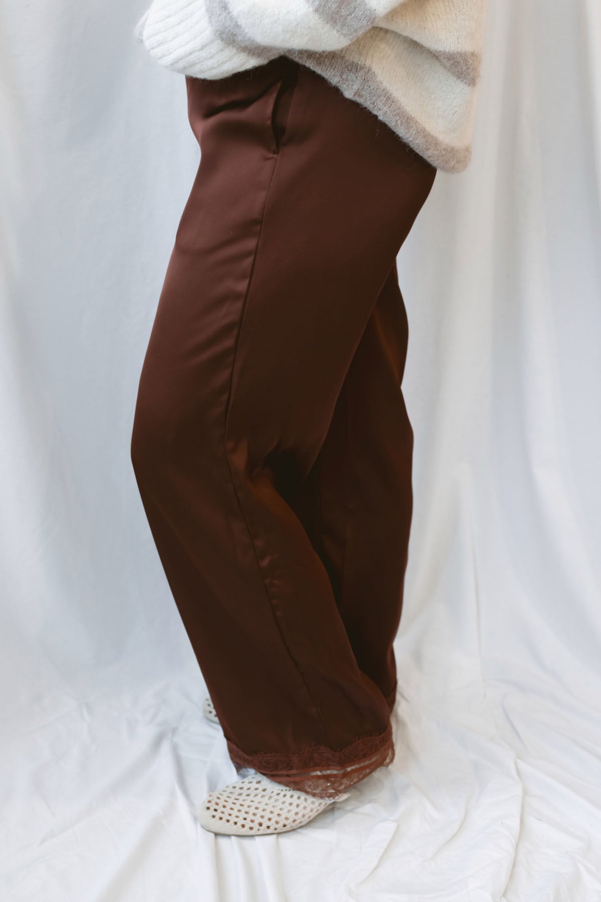 Brown satin wide-leg pants for women featuring delicate lace trim, a mid-waisted silhouette, and a smooth satin finish for elevated everyday styling.