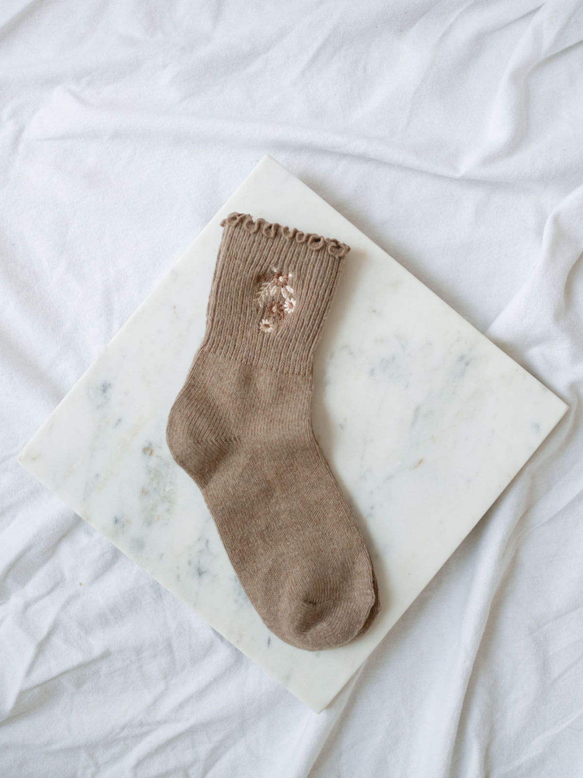 Light coffee socks with floral embroidery detail sitting on marble board.