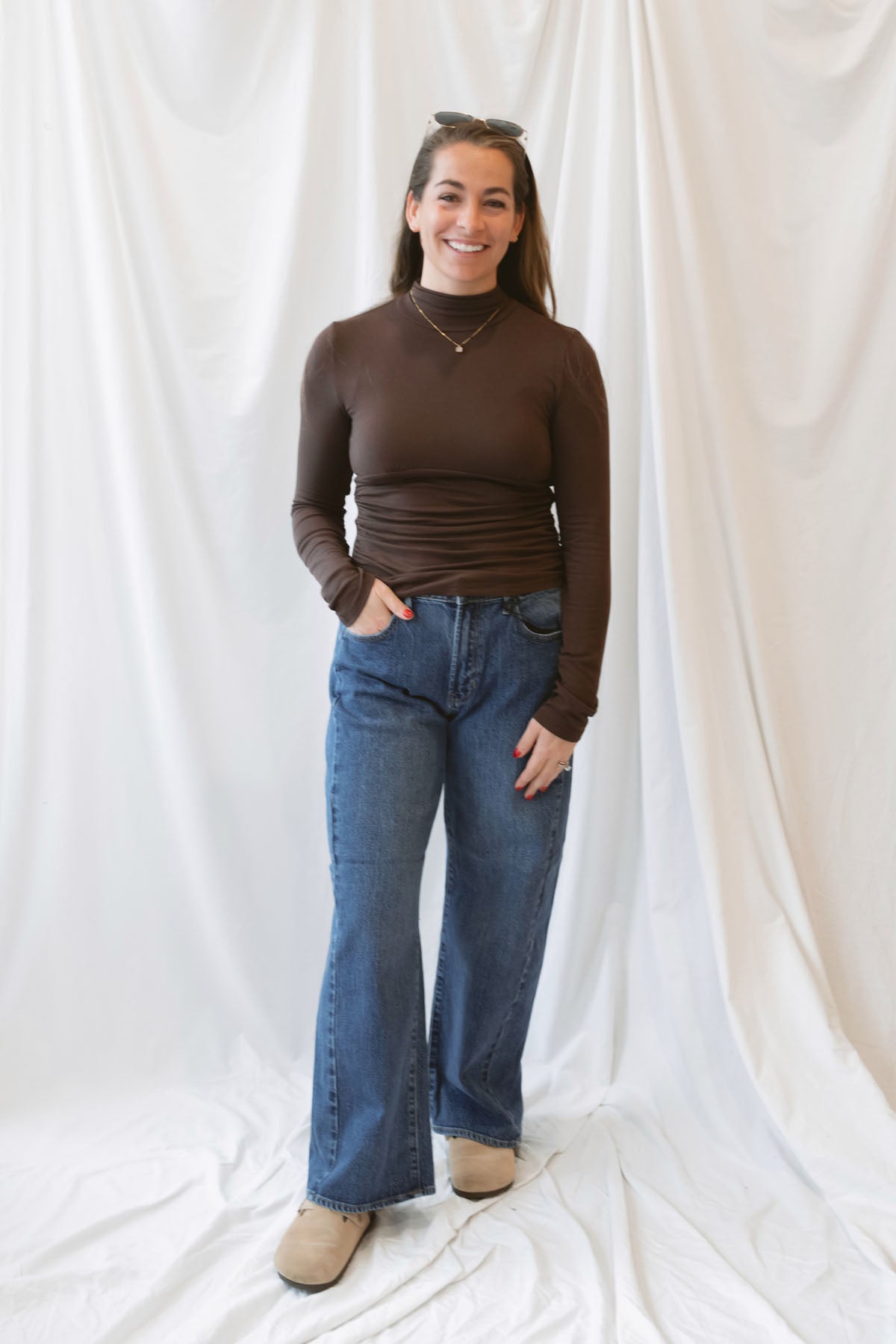 Chocolate brown long-sleeve knit turtleneck top for women featuring ruched waist detailing, a softly shaped silhouette, and an elevated everyday design.