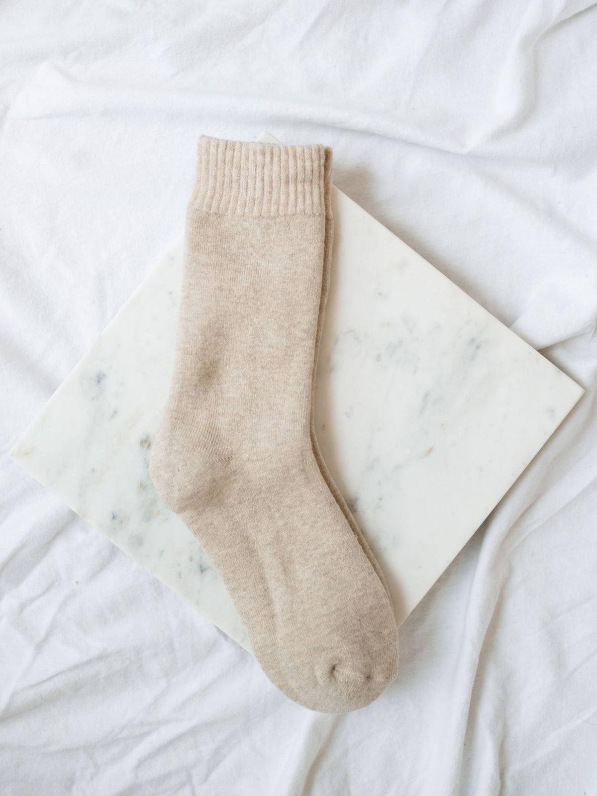 Khaki colored imitation cashmere boot socks laying on a marble board.