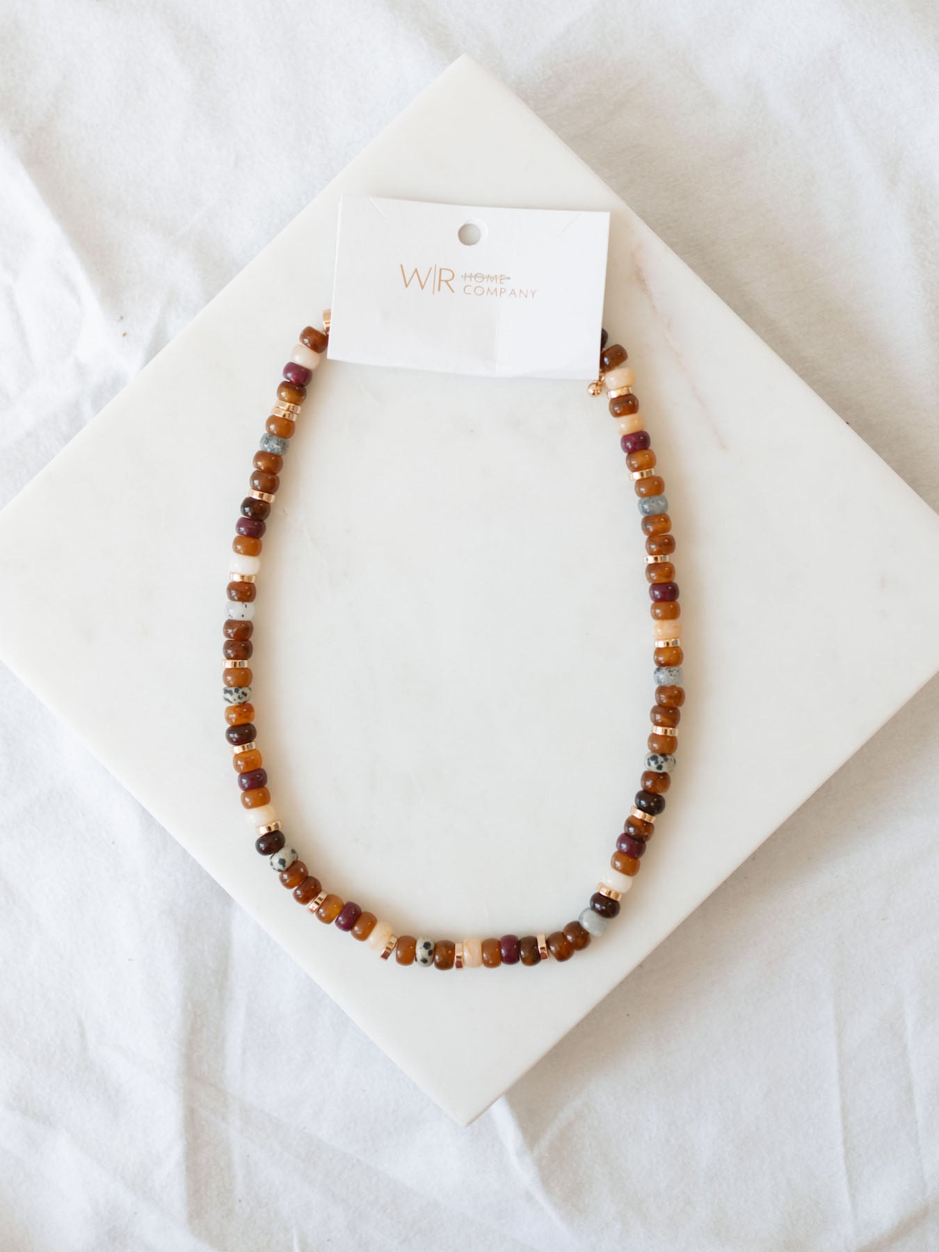 Mixed bead necklace in brown and tan laying on marble board.