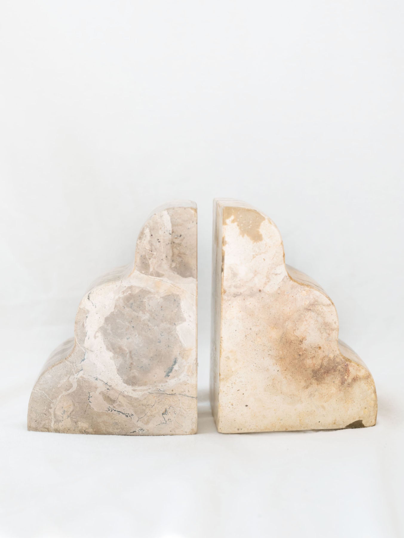 The set of beige marble scalloped edge bookends sitting next to each other with noting between them.