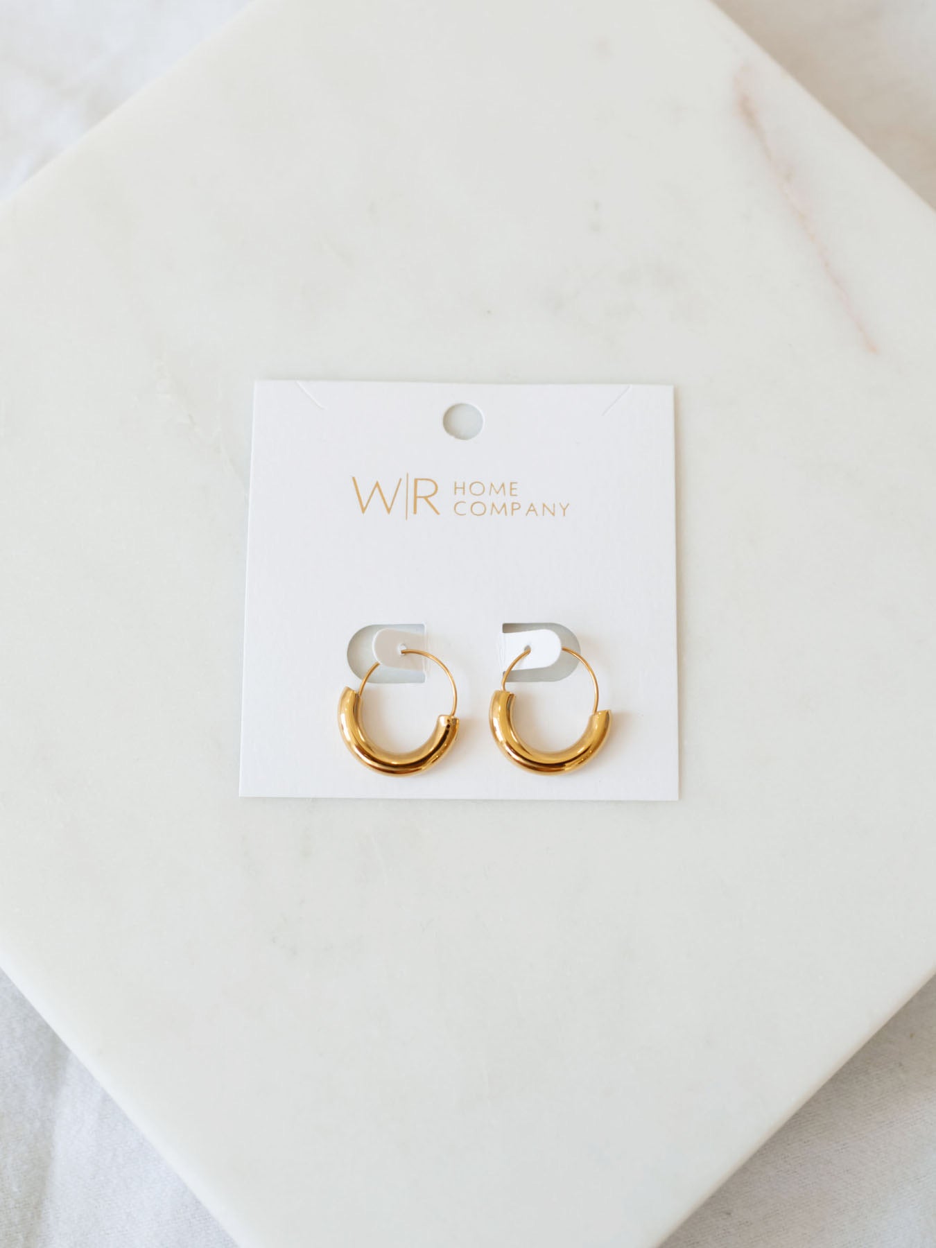 U-shaped gold hoops on white card laying on white marble board.