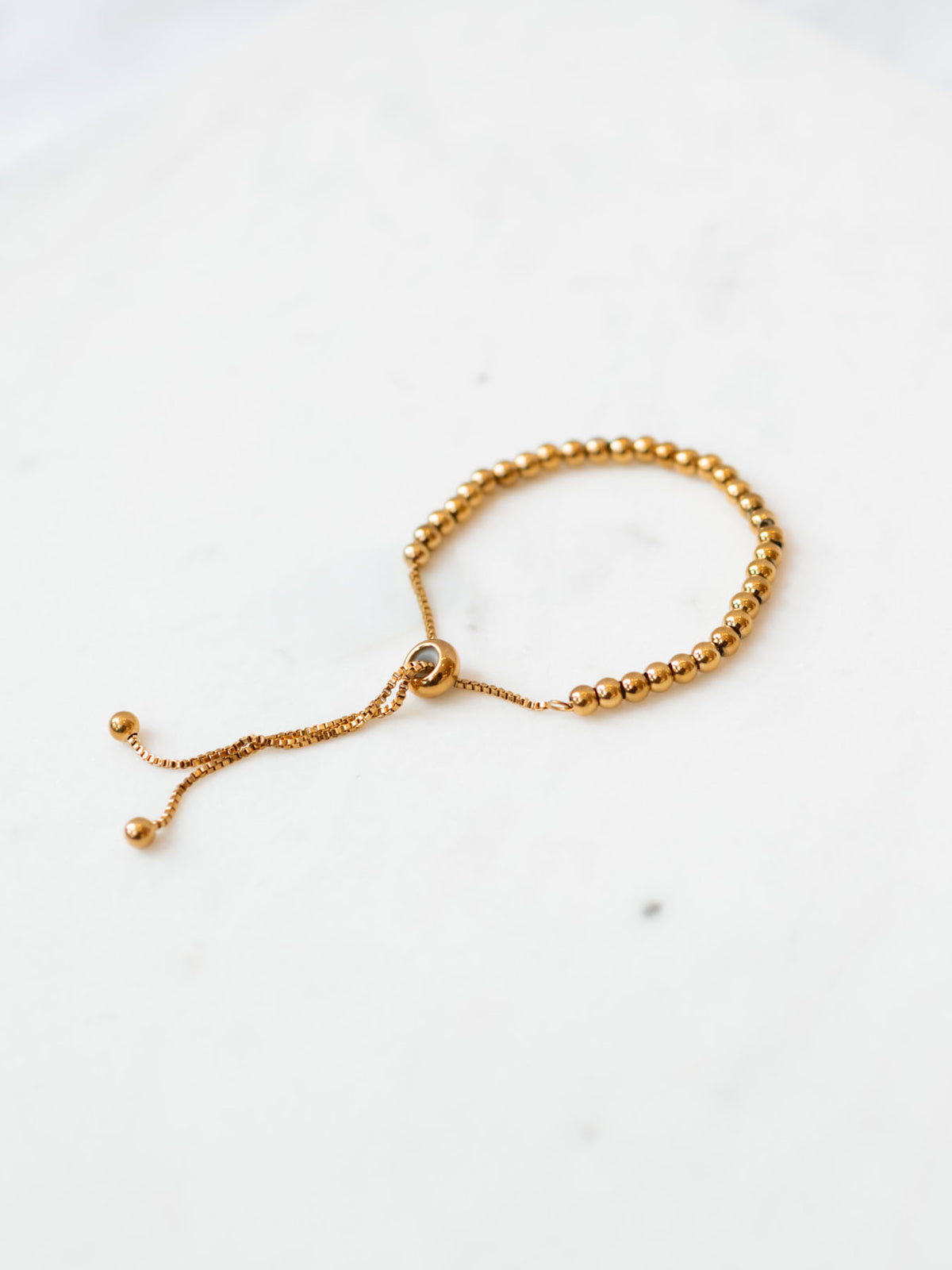 Gold beaded adjustable bracelet in medium size laying on marble board.