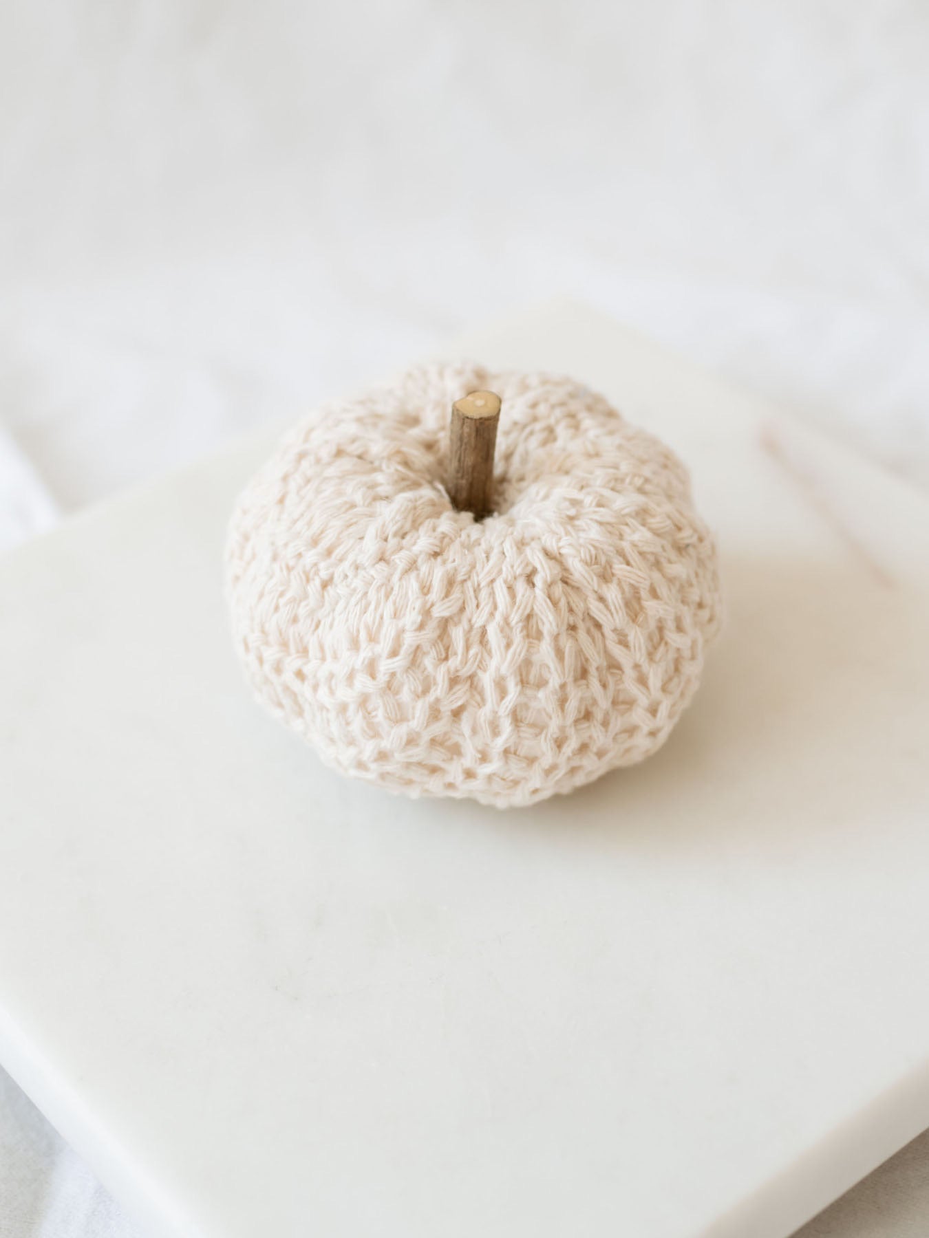 Cream knit filler pumpkin sitting on white marble board.