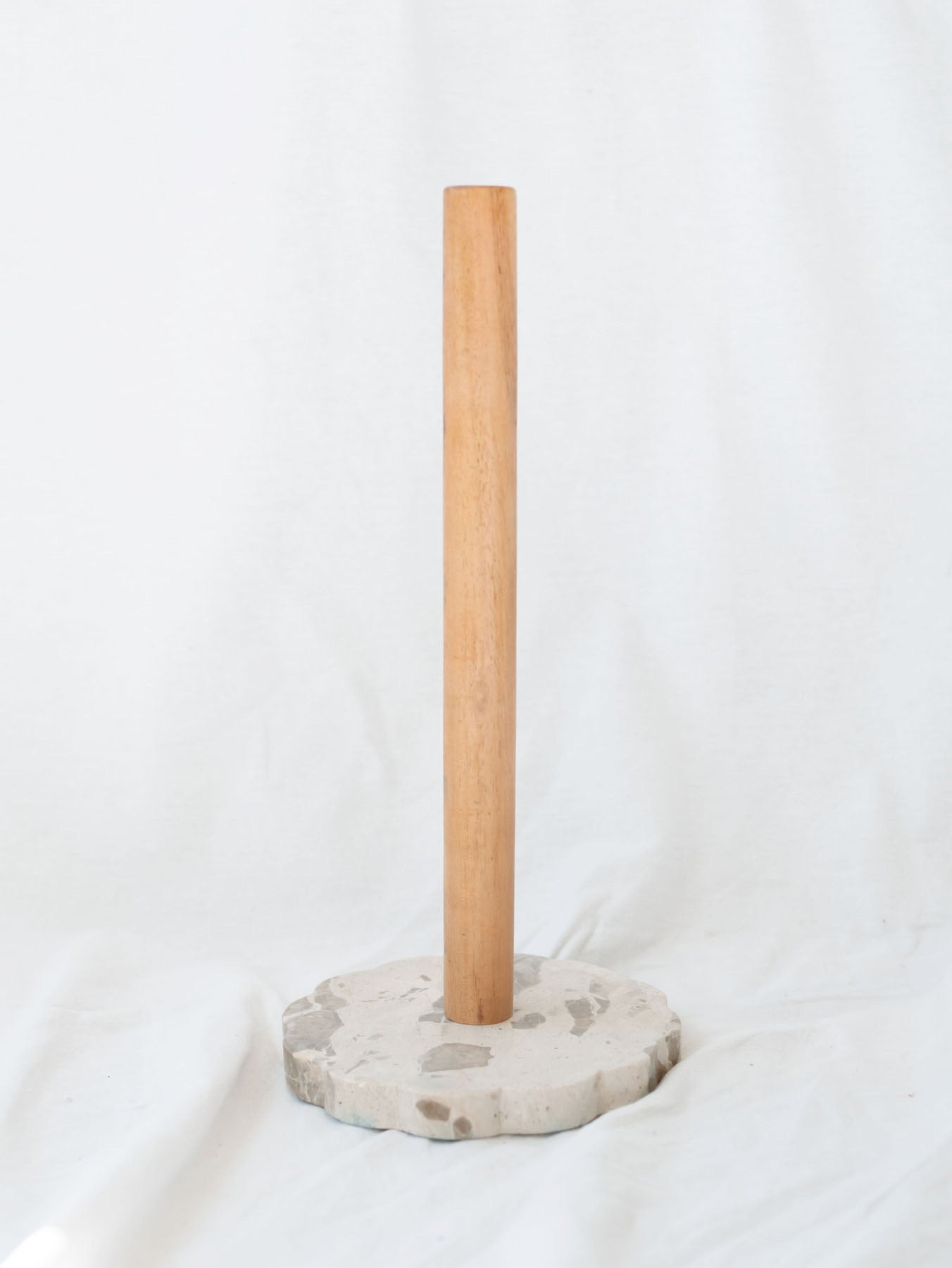 Wood and marble base paper towel holder sitting in front of a white linen backgrop.