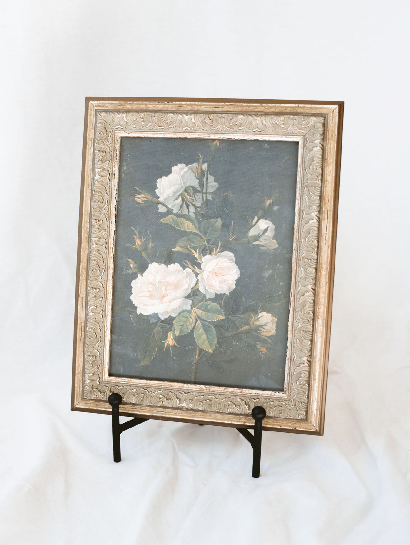Black straight back table top easel holding framed artwork.