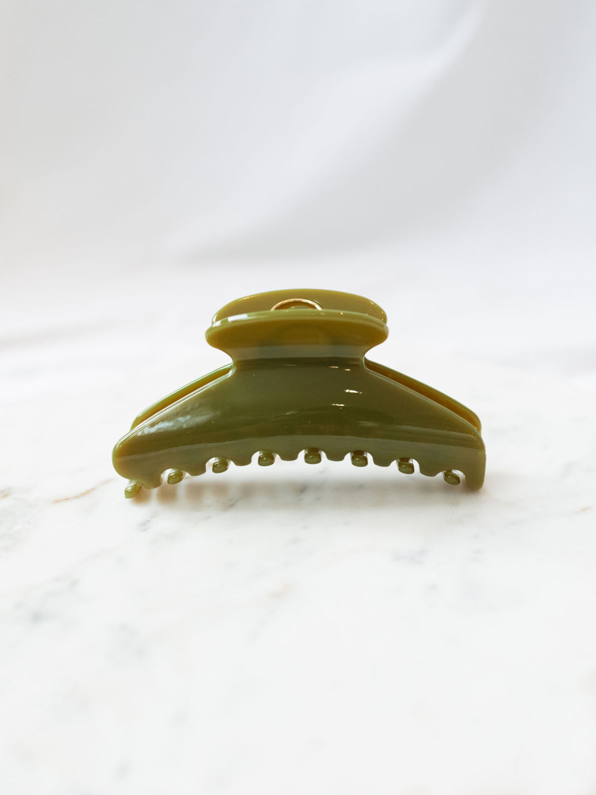 Green glossy fan shaped claw clip sitting on white marble board.
