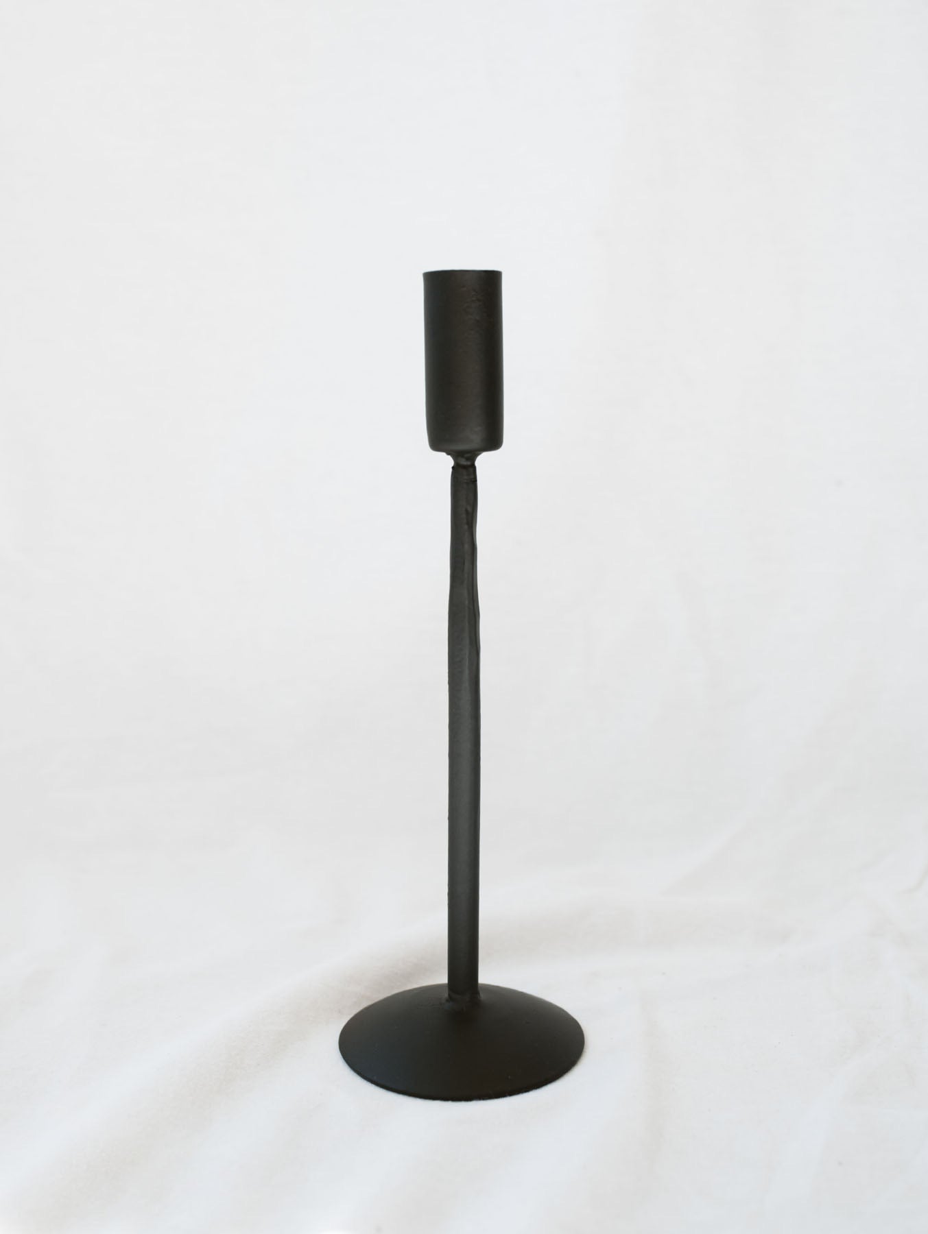 Middle size black candle stick holder sitting on a white linen backdrop. Simple, timeless, and chic home decor option.