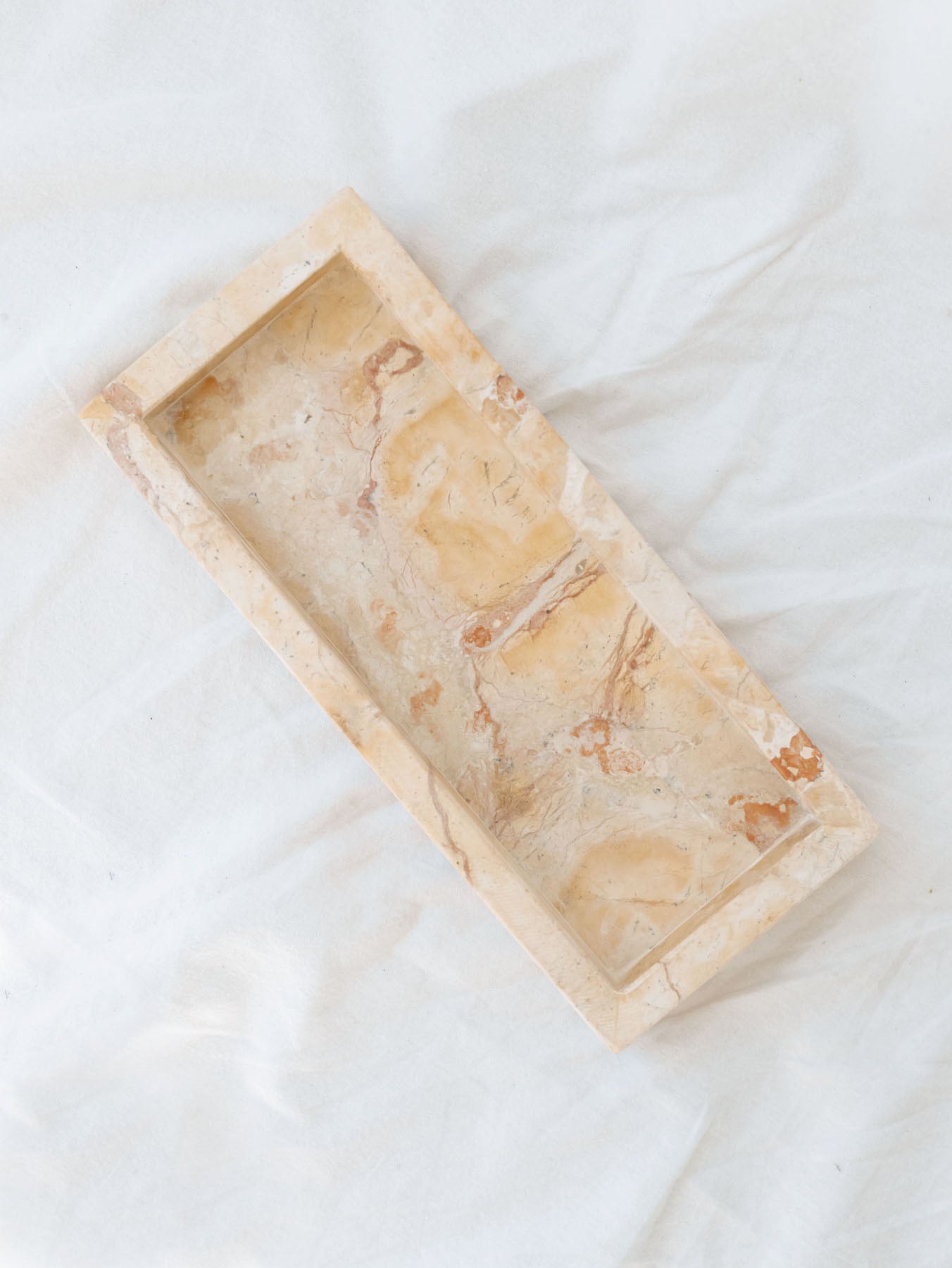 Top view of the beige marbled vanity tray laying on white linen backdrop.