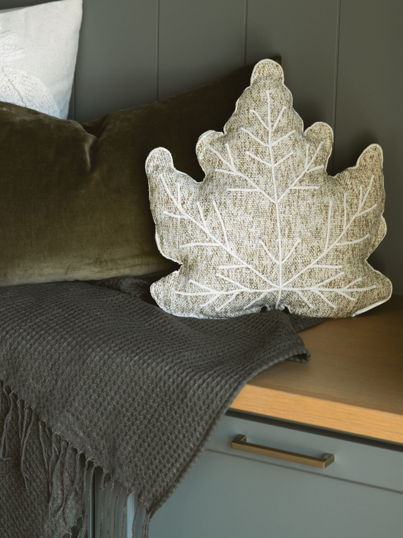 Olive green waffle knit throw blanket styled on a bench with other pillows for a cozy moment.