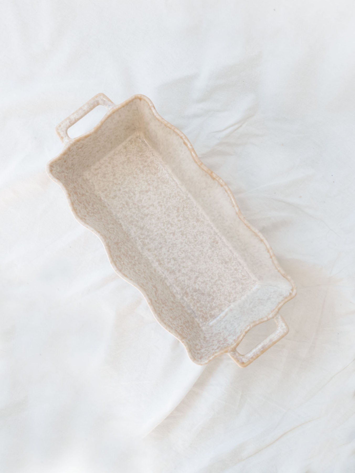 Beige scallop edge baking dish on white linen backdrop.