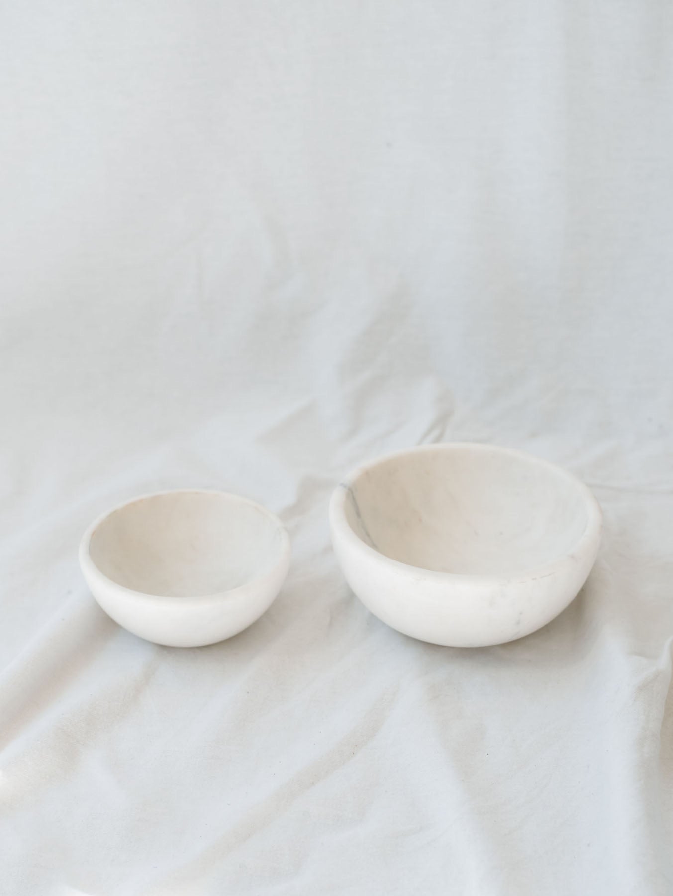 Two different sized marble bowls sitting next to each other in front of a white linen backdrop.