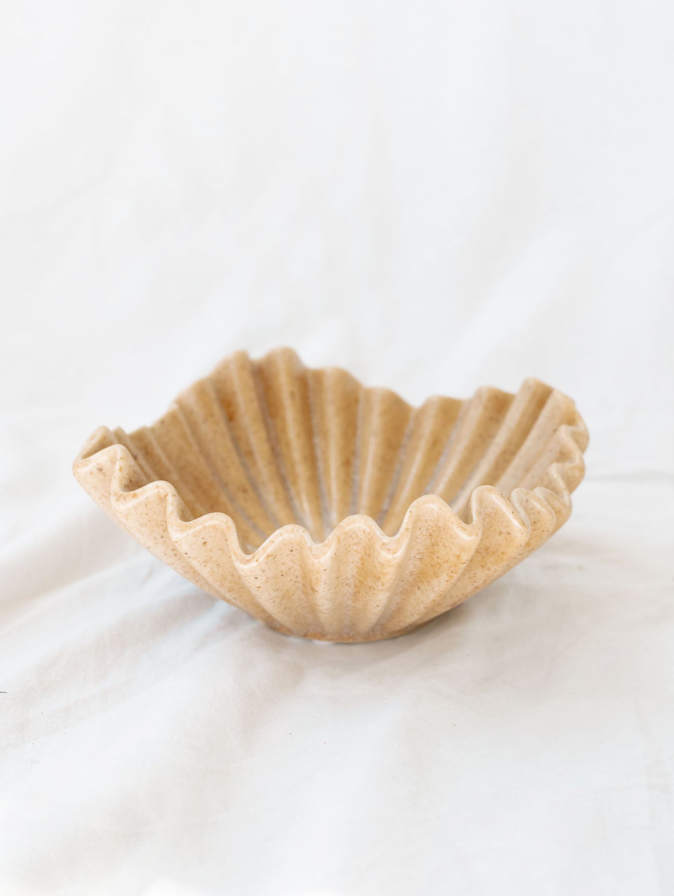 beige ruffle ceramic decorative bowl sitting against a white linen backdrop.