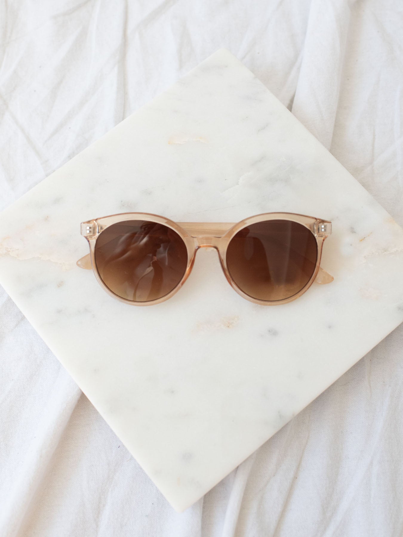 Clear round lens sunglasses laying on marble board.