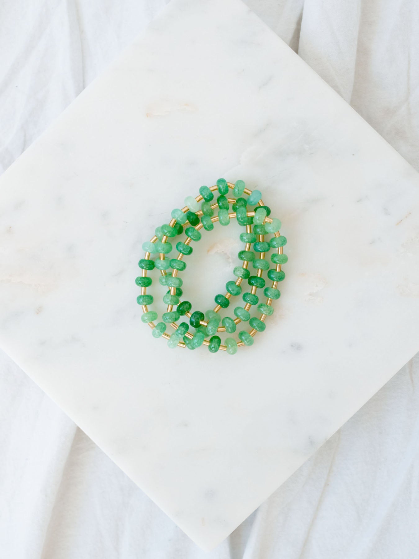 Green and gold beaded bracelet stack laying on a marble board.