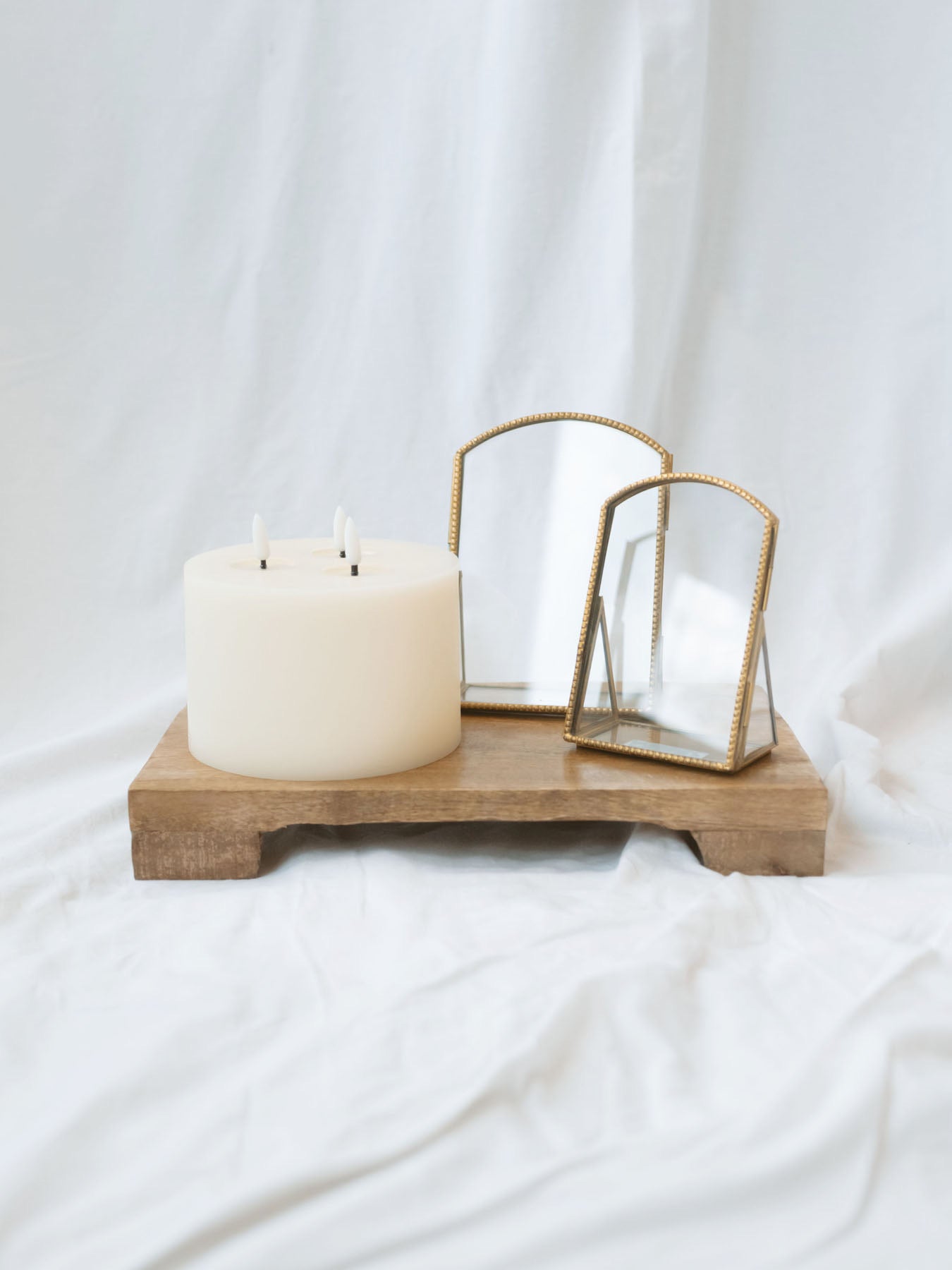 Both arch brass frames sitting next to each other styled with the LED 3 wick candle and sitting on the mango wood pedestal.
