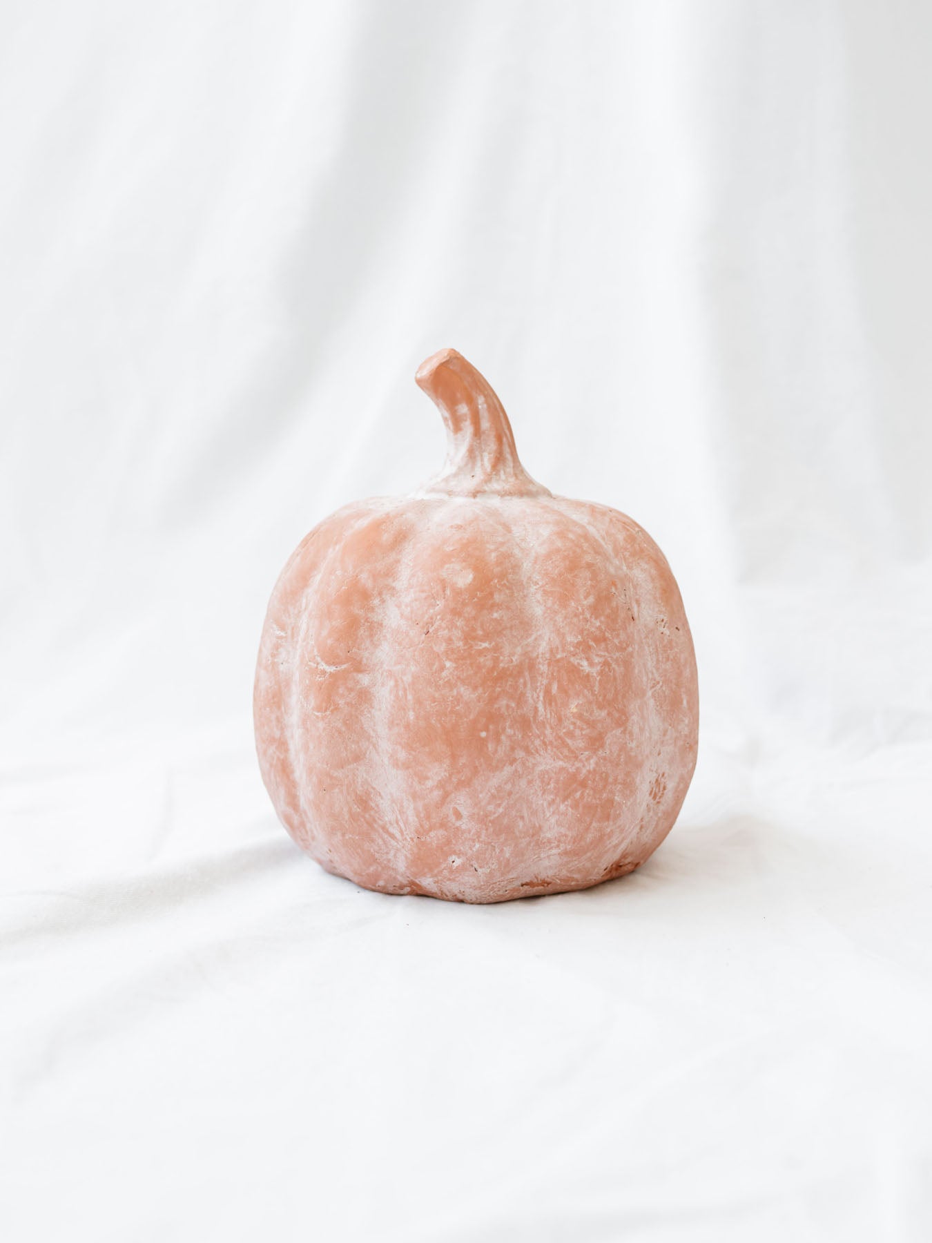 Large size of the terracotta orange pumpkin sitting on white linen backdrop.
